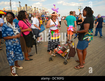 Brooklyn, New York, Stati Uniti d'America. Il 10 agosto 2013. A Coney Island boardwalk, IVELIZ BALTAZAR da Harrison, New Jersey, indossa un palloncino colorato cappello e grembiule, come ella crea forme a palloncino per un bambino ragazza. Foto Stock