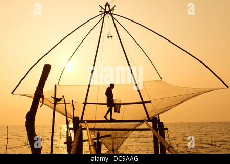 Fisherman tenendo un guadino in un cinese rete da pesca di sunrise Foto Stock