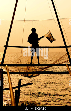 Fisherman tenendo un guadino davanti a un cinese rete da pesca di sunrise Foto Stock