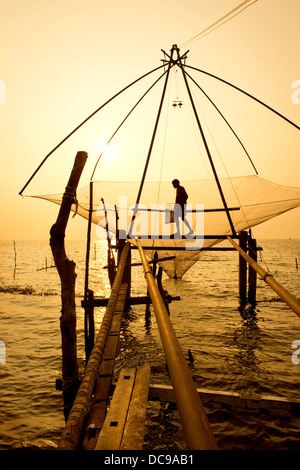 Fisherman tenendo un guadino in un cinese rete da pesca di sunrise Foto Stock