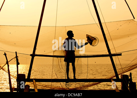 Fisherman tenendo un guadino davanti a un cinese rete da pesca di sunrise Foto Stock