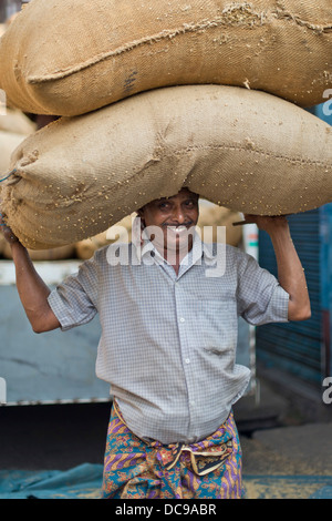 Uomo che porta due sacchi riempiti con spezie sulla sua testa Foto Stock