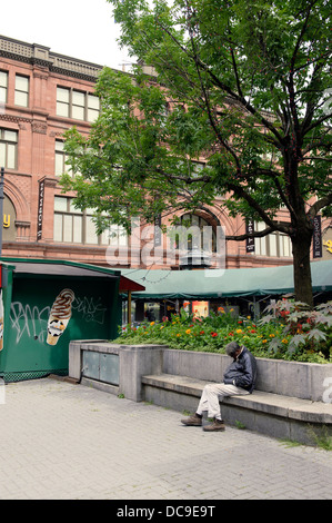 Senzatetto uomo seduto addormentato su un banco di cemento nel centro di Montreal. Foto Stock