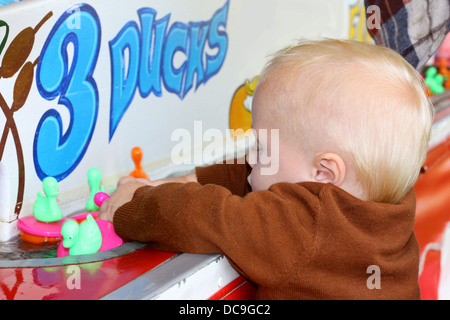 Un simpatico baby boy è afferrando una manciata di anatre come galleggiano da durante un carnevale estivo gioco di anatra Foto Stock