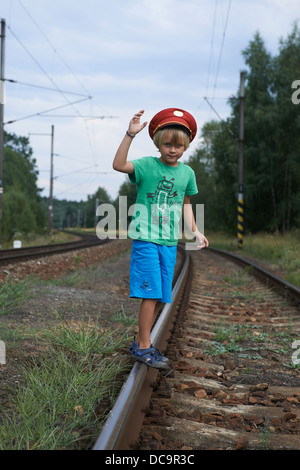 Bambino ragazzo biondo con Train Dispatcher cappuccio della riproduzione nella stazione ferroviaria Foto Stock