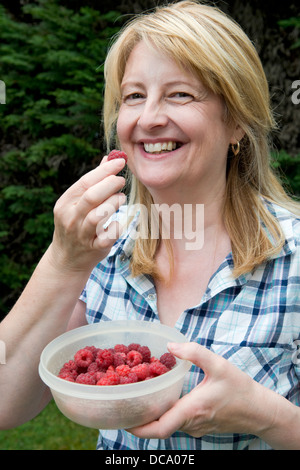 Sorridente donna caucasica mangiare appena raccolto cresciuto in casa lamponi, dal giardino in Bristol, Regno Unito Foto Stock