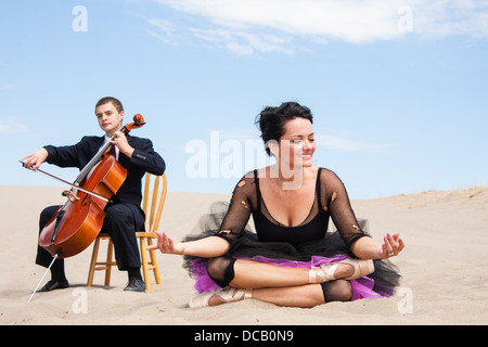 Una ballerina in un rilassante yoga pone nel deserto-chiude gli occhi. un violoncellista Suona un assolo di sogno in background. Foto Stock