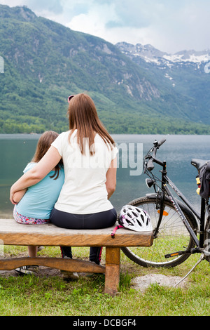 Madre e figlia insieme seduta su una panca in legno dal lago di Bohinj, Slovenia Gorenjska. Foto Stock