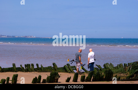 Resti di legno storico relitto barca sulla spiaggia di Seaton Carew Hartlepool con due persone con i rivelatori di metallo. Foto Stock