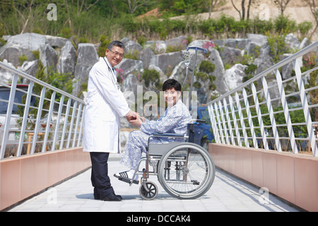 Un medico tenendo le mani con il paziente seduto su una sedia a rotelle Foto Stock