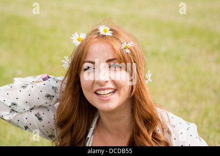 Un orizzontale, immagine a colori di un felice e giovane donna sorridente con lunghi capelli rossi, con una catena a margherita nei suoi capelli Foto Stock