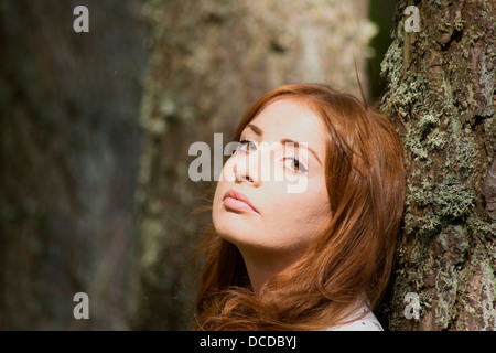 Un'immagine orizzontale di una giovane e bella donna appoggiato a un albero Foto Stock