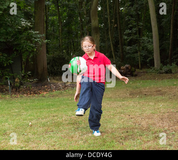 Giovane ragazza calci ad un pallone da calcio in giro per iarda posteriore Foto Stock