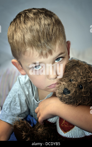 Triste ragazzino con un livido sotto il suo occhio che impugnano un orsacchiotto di peluche. La violenza domestica. Foto Stock