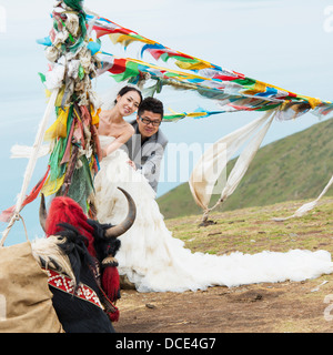 Sposa e lo sposo che pongono sotto bandiere di preghiera vola nel vento; Shannan, Tibet, Xizang, Cina Foto Stock