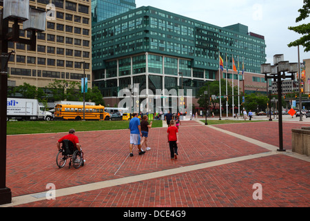 Uomo in sedia a rotelle su un ampio marciapiede vicino al porto interno, Renaissance Harbour Place Hotel in background, Baltimore, Maryland, Stati Uniti d'America Foto Stock