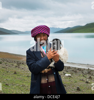 Cina, Xizang, Tibet, Shannan, donna holding, capra di piccole dimensioni sul bordo del lago sacro Foto Stock