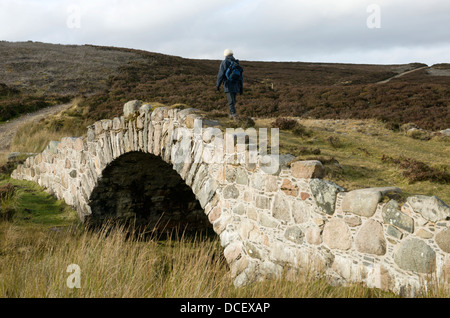 Un viandante attraversa il ponte Delavine sulla vecchia strada militare nel Parco Nazionale di Cairngorms in Scozia Foto Stock