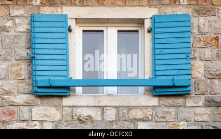 Finestra in legno con blue open jalousies in grigio vecchio muro di pietra Foto Stock