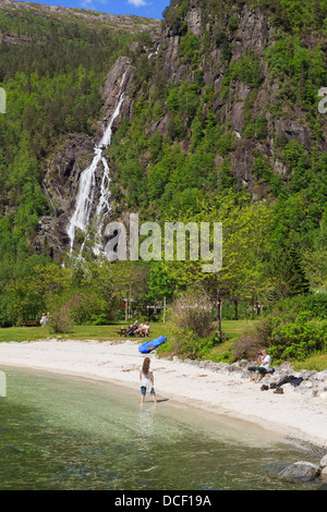 Tourist in posa sulla spiaggia da una cascata nel villaggio alla fine del fiordo Mofjorden. Mo, Modalen, Hordaland, Norvegia e Scandinavia Foto Stock