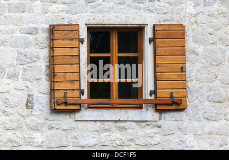 Finestra in legno con open jalousies in grigio vecchio muro di pietra Foto Stock