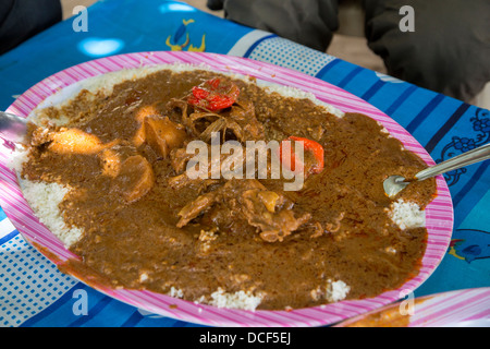 Anacardi con spezzatino di pollo con peperoni e riso. La gente attorno al tavolo di mangiare da un piatto comune. Il Gambia. Foto Stock