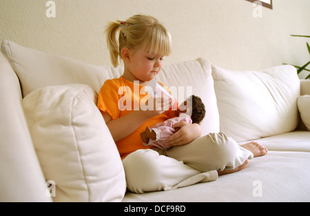 Bambina dà la sua bambola un biberon Foto Stock