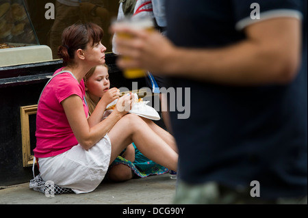 Donna e bambina mangiando pesce e patatine seduto sul marciapiede tra la folla durante il Brecon Jazz Festival 2013 Foto Stock