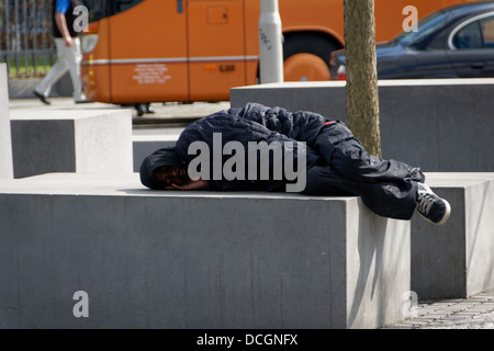 Un senzatetto uomo dorme sul campo di stele del monumento commemorativo dell'Olocausto in Berlin-Mitte Foto Stock