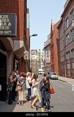 Gli uomini e le donne in piedi al di fuori di un wine bar nella città di Londra di bere e fumare England Regno Unito Foto Stock