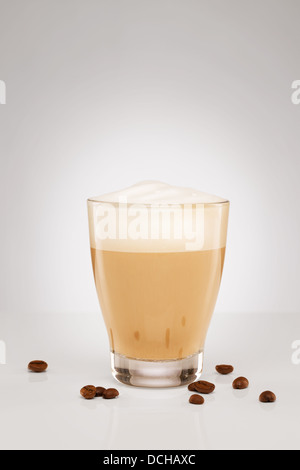 Cappuccino con schiuma di latte in un piccolo bicchiere con i chicchi di caffè su sfondo grigio Foto Stock