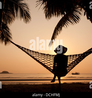 Donna in amaca godersi il tramonto sulla spiaggia Foto Stock