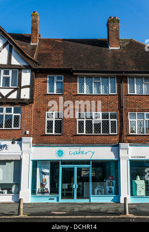 Boutique cakery shop (torte personalizzate per ordine), con appartamenti sopra, sul villaggio di Banstead High Street, su di una tranquilla domenica mattina nel Surrey, Inghilterra, Regno Unito. Foto Stock