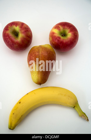 Due mele, una pera e una banana guardando come una faccina triste. Foto Stock