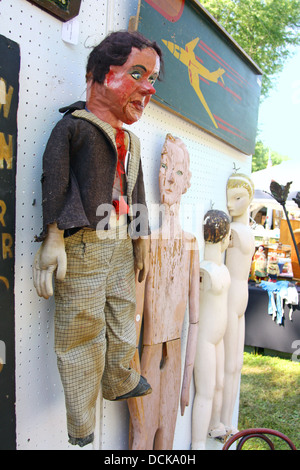 Un dipinto e vestito di legno vintage ventriloquo fantoccio appeso su una parete accanto ad altre bambole in legno e arte in un mercato delle pulci. Foto Stock