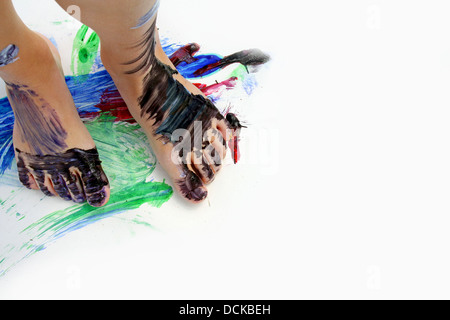 Vicino a un piccolo bambino i piedi che sono coperti di vernice, in piedi su un grande vuoto di carta bianca con dipinti colorati. Foto Stock
