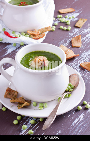 Verde zuppa di piselli servito in tazza bianca e guarnita con cracker di segale Foto Stock