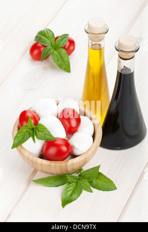 Mozzarella con pomodori ciliegia, basilico e olio di oliva con aceto bianco sul tavolo di legno Foto Stock