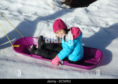 Giovane ragazza asiatica sulla slitta nella neve Foto Stock