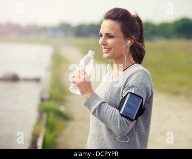 Donna sorridente runner mentre si beve acqua in bottiglia Foto Stock