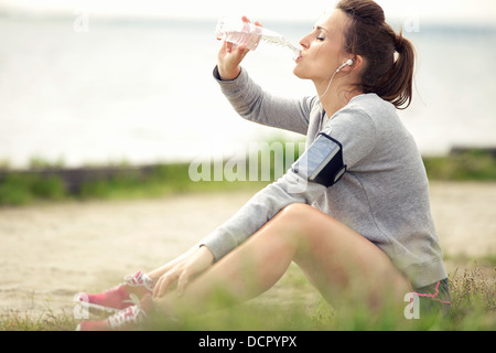 Stanchi del pareggiatore femmina seduto sull'erba e di bere acqua in bottiglia Foto Stock