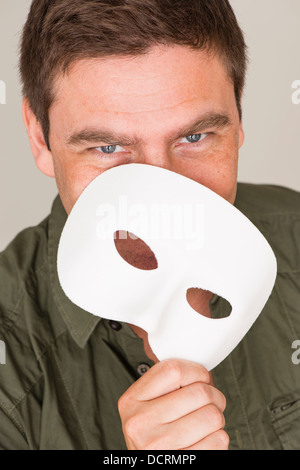 Felice e uomo sorridente di nascondersi dietro la maschera bianca Foto Stock