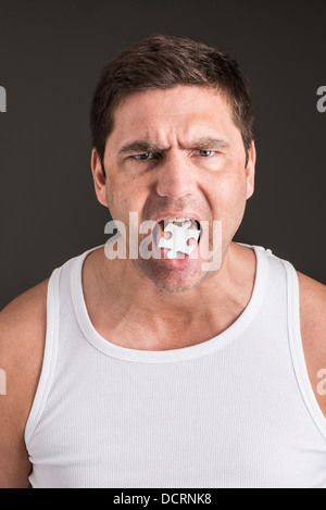 Frustrati e l'uomo arrabbiato con un pezzo di puzzle sulla punta della sua lingua. Immagine concettuale di problem solving e stress. Foto Stock