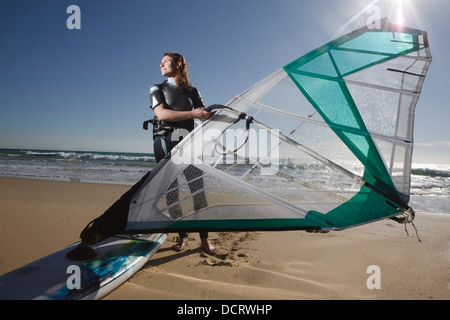 Giovane donna posa con la tavola a vela sulla spiaggia Foto Stock