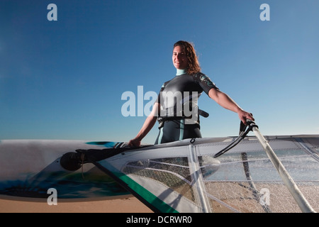 Giovane donna posa con la tavola a vela sulla spiaggia Foto Stock