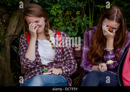 Due sorelle, adolescente e giovane adulto, seduti su una panchina e ridere. Foto Stock