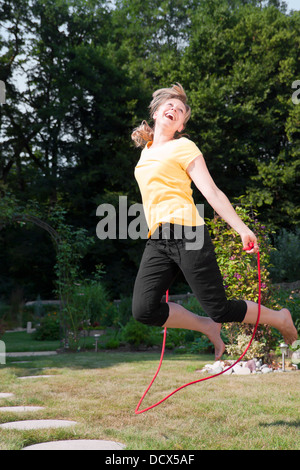 Giovane donna salto con la corda in giardino Foto Stock