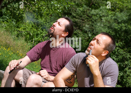Due uomini fumatori e-sigarette nella natura Foto Stock