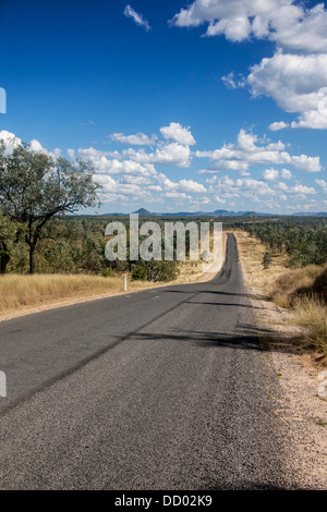 Outback / bussola / country road con alberi di eucalipto su entrambi i lati e le montagne in distanza e auto sulla strada del Queensland, Australia Foto Stock