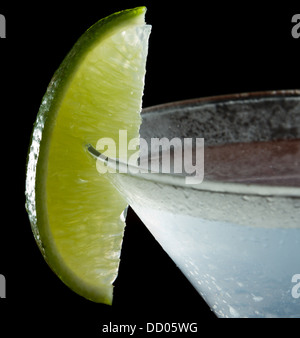 Uno spicchio di lime sul bordo di una coppetta Martini utilizzato come guarnire isolata su uno sfondo nero Foto Stock